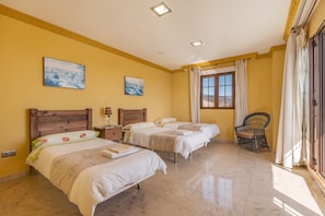 A hotel room with two beds, a window with curtains, a chair, and two paintings on the wall.
