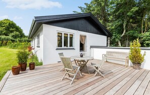Uma casa branca com telhado preto, deck de madeira e um jardim.
