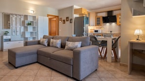 Una sala de estar moderna con un sofá seccional, un comedor con mesa y sillas, y una cocina con armarios y electrodomésticos.