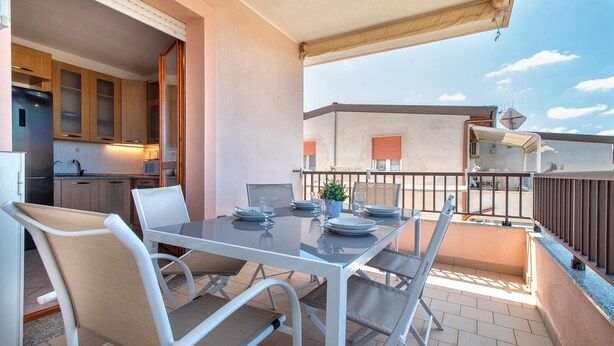 Un balcón con mesa lista para comer, una zona de cocina y vistas del edificio de enfrente.