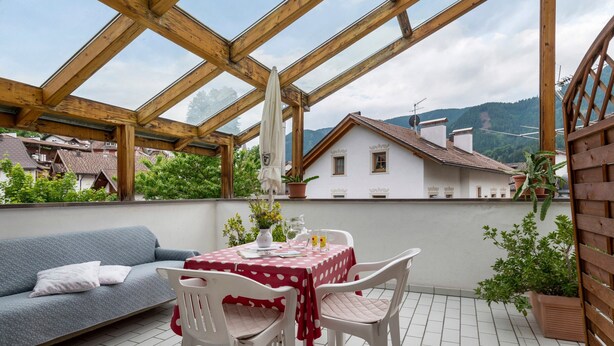 En overdækket terrasse med et bord, stole, en sofa og plantekasser.
