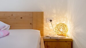 En pænt redt seng med et trægavl, et natbord med en lampe, og en stikkontakt på væggen.
