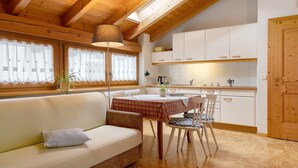 A cozy kitchen with a wooden ceiling, white cabinets, a dining table with chairs, and a sofa with a cushion. - Apartment 'Appartment Love' with Mountain View, Shared Garden and Wi-Fi (Sarnthein)