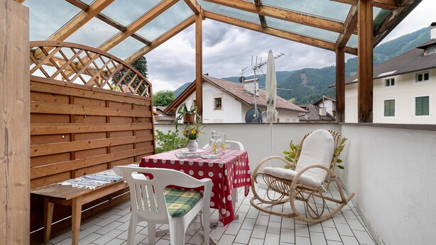A covered patio with a wooden bench, a table with a red tablecloth, and a wicker chair. - Apartment 'Appartment Love' with Mountain View, Shared Garden and Wi-Fi (Sarnthein)