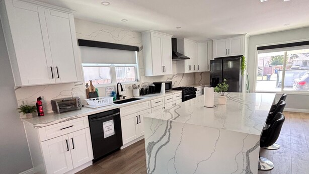 A modern kitchen with white cabinetry, a marble countertop, and a stainless steel refrigerator. - Seasun Hostel (Northridge)