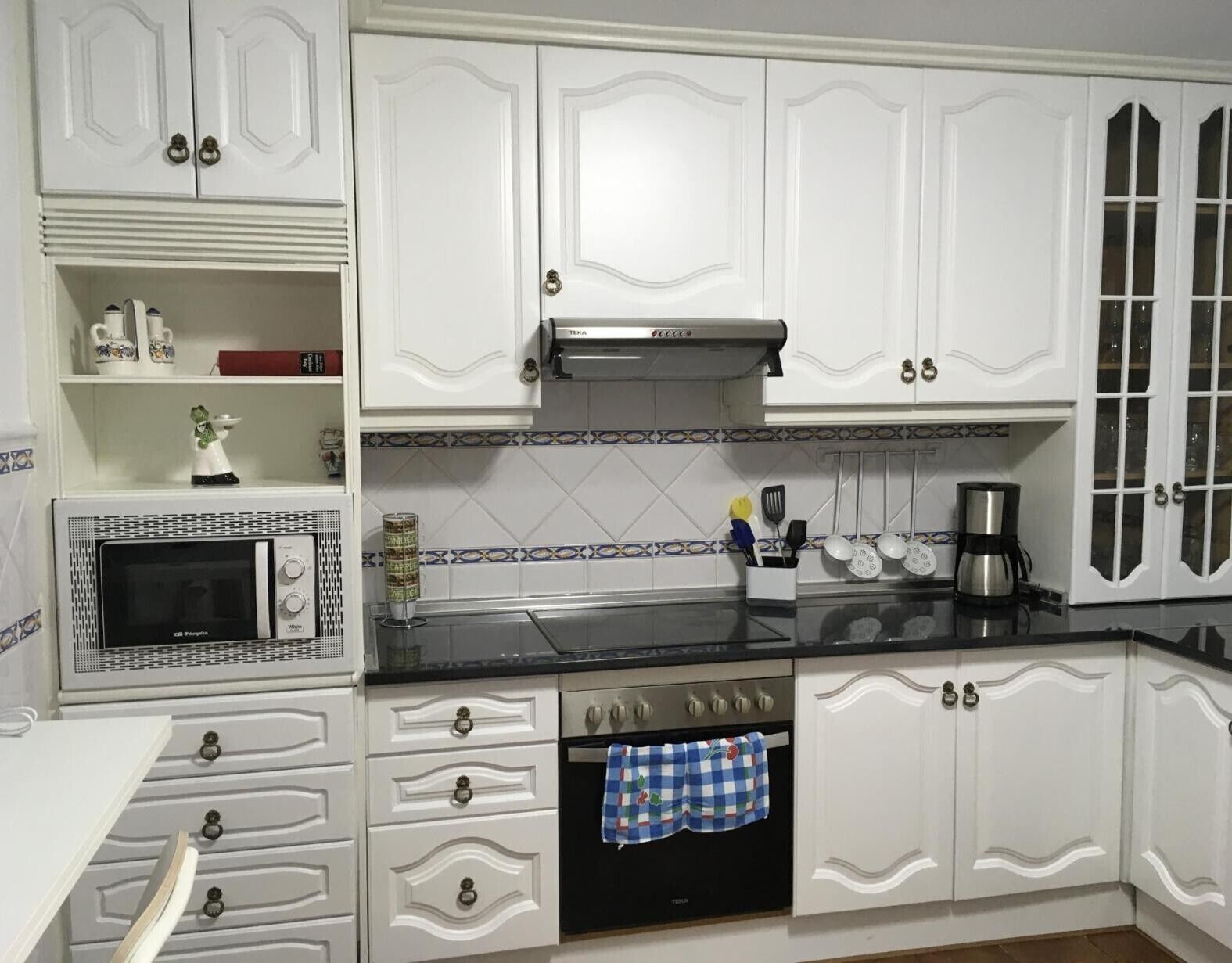 A kitchen with white cabinetry, a microwave, an oven, and a coffee maker.
