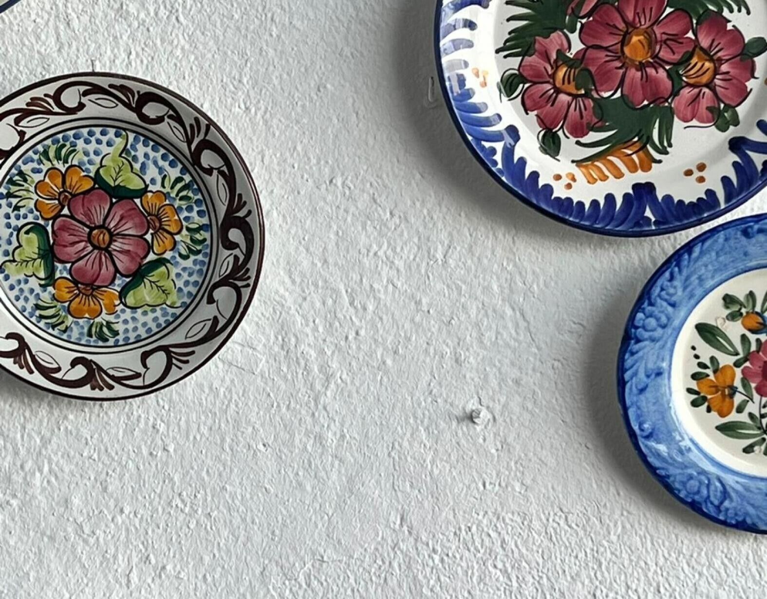 Three ceramic plates with floral designs on a textured wall.