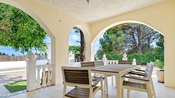 Ein überdachter Patio-Bereich mit Tisch und Stühlen, umgeben von Bögen und Blick ins Freie.