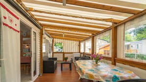 Eine überdachte Terrasse mit Holzboden, einem Tisch mit bunten Tischdecken und Blick auf eine Wohngegend.