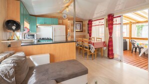 Eine kompakte Küche mit Kühlschrank, Mikrowelle und Herd. Es gibt einen Essbereich mit Tisch und Stühlen sowie ein Sofa im Wohnbereich.