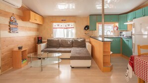 Eine kompakte Küche mit Holzausstattung, ein Essbereich mit Glastisch und eine Sitzecke mit einer Couch.