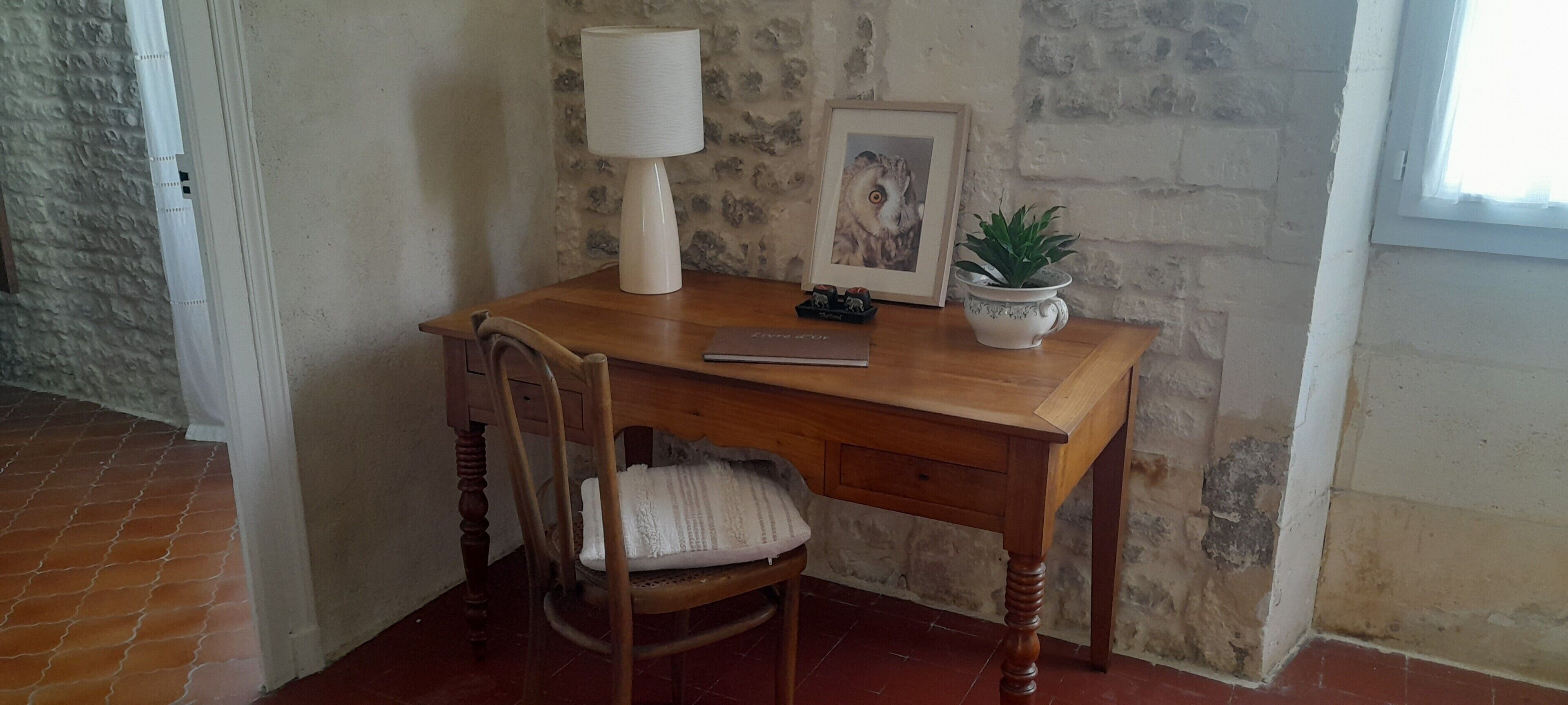 A wooden desk with a lamp, a framed picture, and a potted plant.