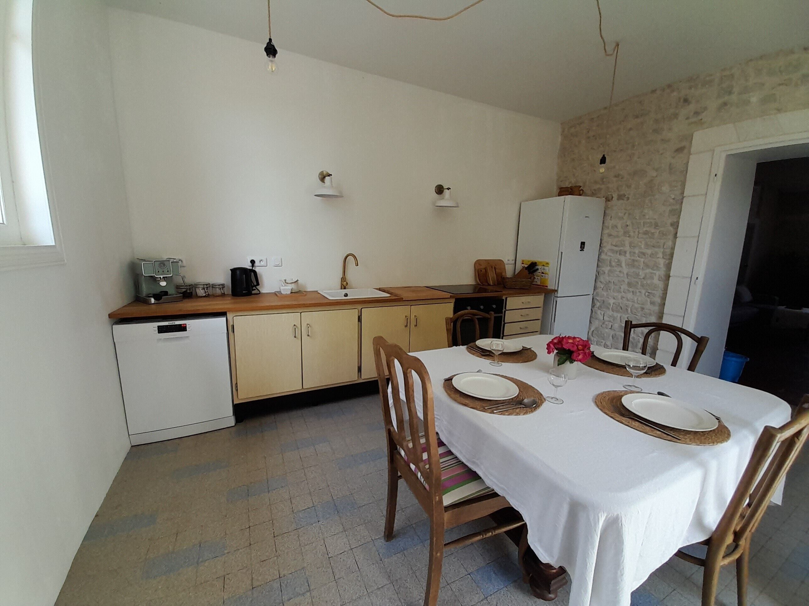 Eine kleine Küche mit Spüle, Kaffeemaschine und Kühlschrank. Ein Esstisch ist mit Tellern und Gläsern gedeckt.