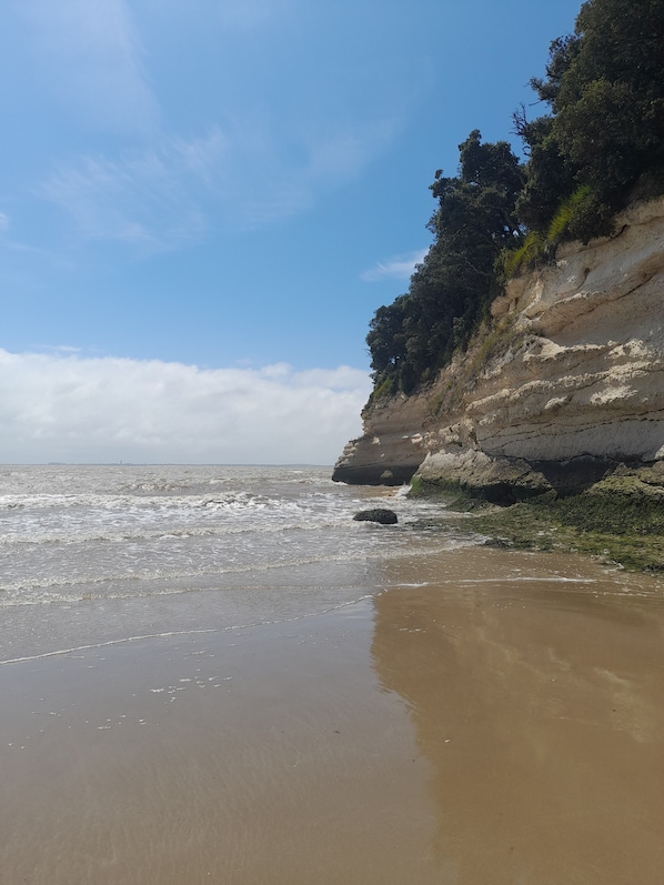A beach with a rocky cliff and waves.