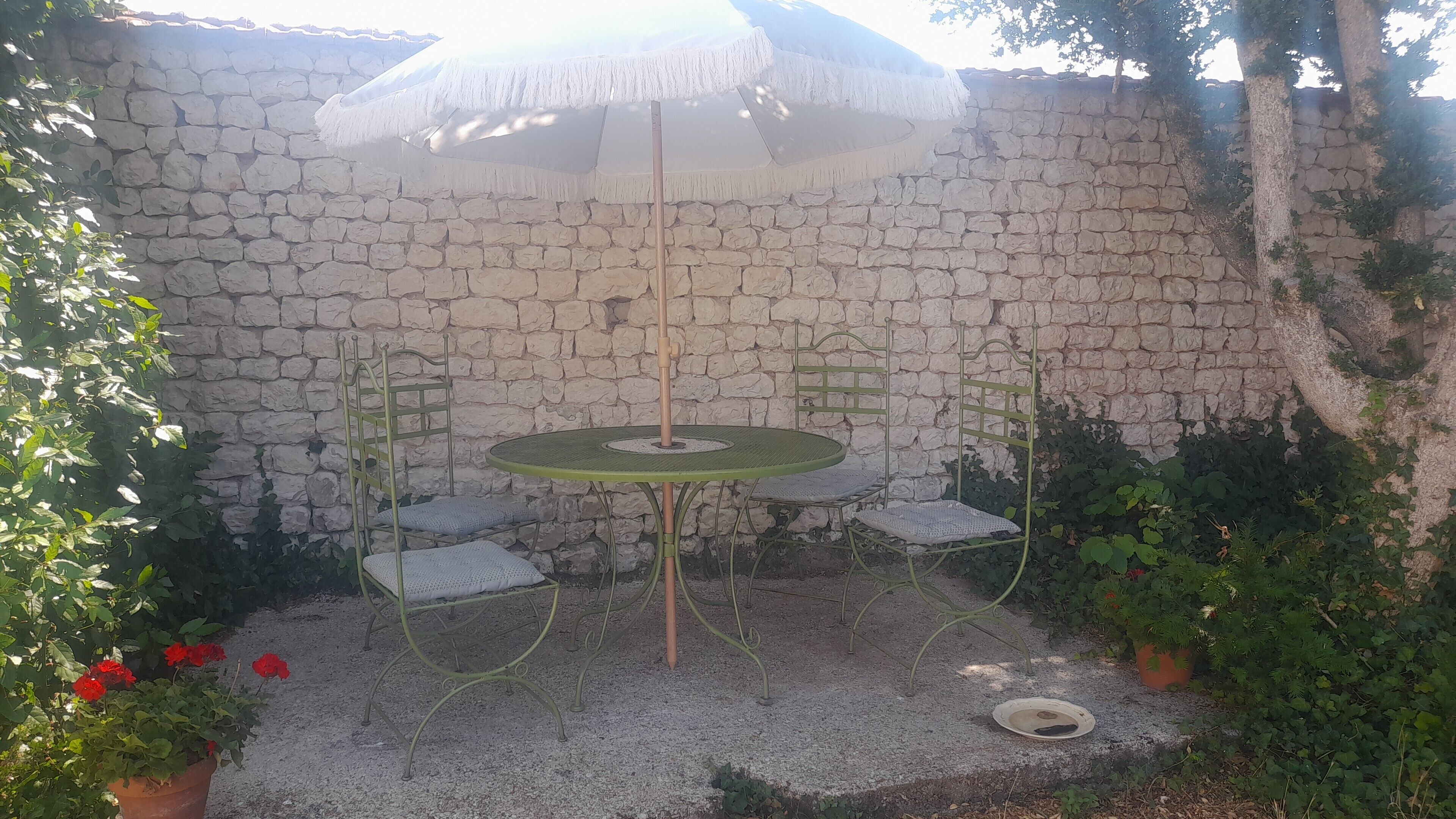 Un espace patio agrémenté d’un mur en pierre, d’une table ronde, de deux chaises et d’un parasol.