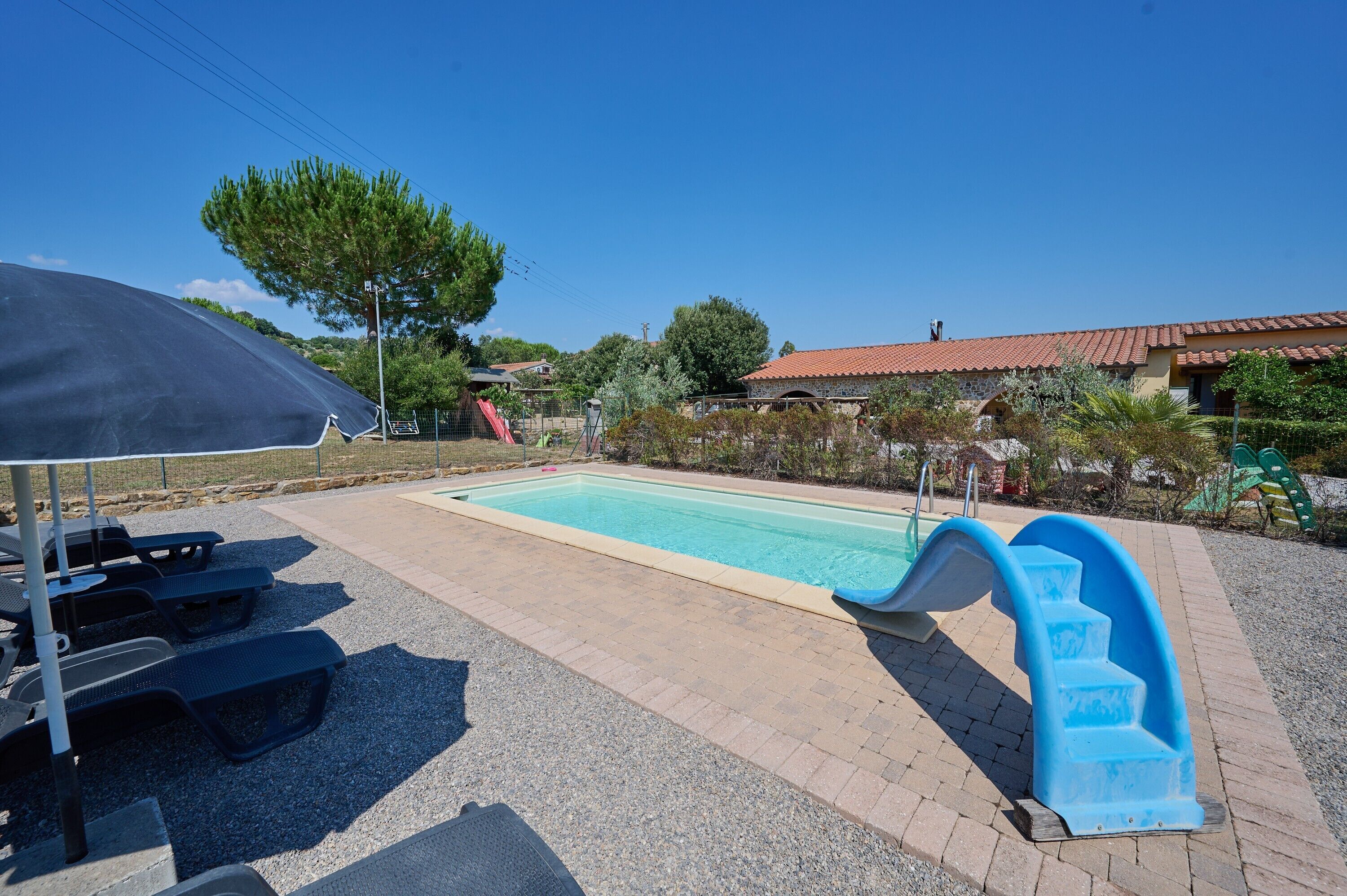 Una piscina con tobogán, mesas de picnic y un área cubierta.