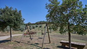 Ein Park mit einer Schaukel, einer Steinsitzbank und einem Feldweg.