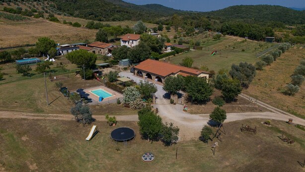 Ein Luftbild eines ländlichen Anwesens mit Swimmingpool, einem runden Trampolin und einer gepflasterten Einfahrt, die zu einem Haus mit rotem Ziegeldach führt.