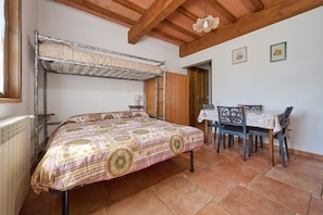 Una habitación con literas, una mesa de comedor con sillas, un radiador y vigas de madera en el techo.