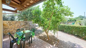 Eine Terrass mit Steinmauern, einer Holzpergola und einem Tisch mit Stühlen.