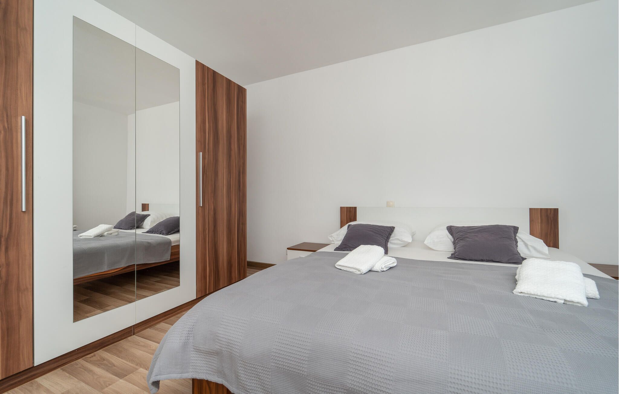 A modern bedroom with a large wardrobe, a bed with grey bedding, and a wooden headboard.