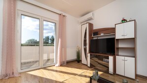 Un salon moderne doté d’une porte-fenêtre coulissante, d’un téléviseur à écran plat, de planchers en bois et d’étagères intégrées.