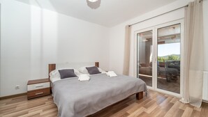 Une chambre avec un lit, une table de chevet, une porte-fenêtre coulissante donnant sur un balcon et un plancher en bois.