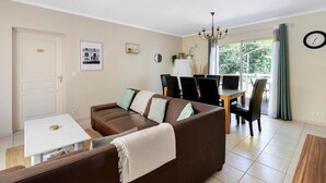 En stue med en brun sofa, et hvidt bord og et spiseområde med stole og en lysekrone.