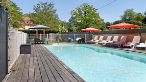 En swimmingpool med liggestole og parasoller, omgivet af et hegn og træer.