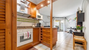 A kitchen with wooden cabinets, a microwave, an oven, and a small wooden stool. - Apartment 'Bumbai' with Shared Pool, Private Garden and Air Conditioning (Creixell)
