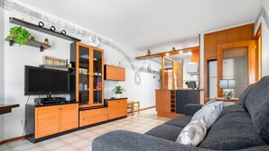 A modern living room with a sofa, TV, wooden cabinets, and a kitchen area. - Apartment 'Bumbai' with Shared Pool, Private Garden and Air Conditioning (Creixell)
