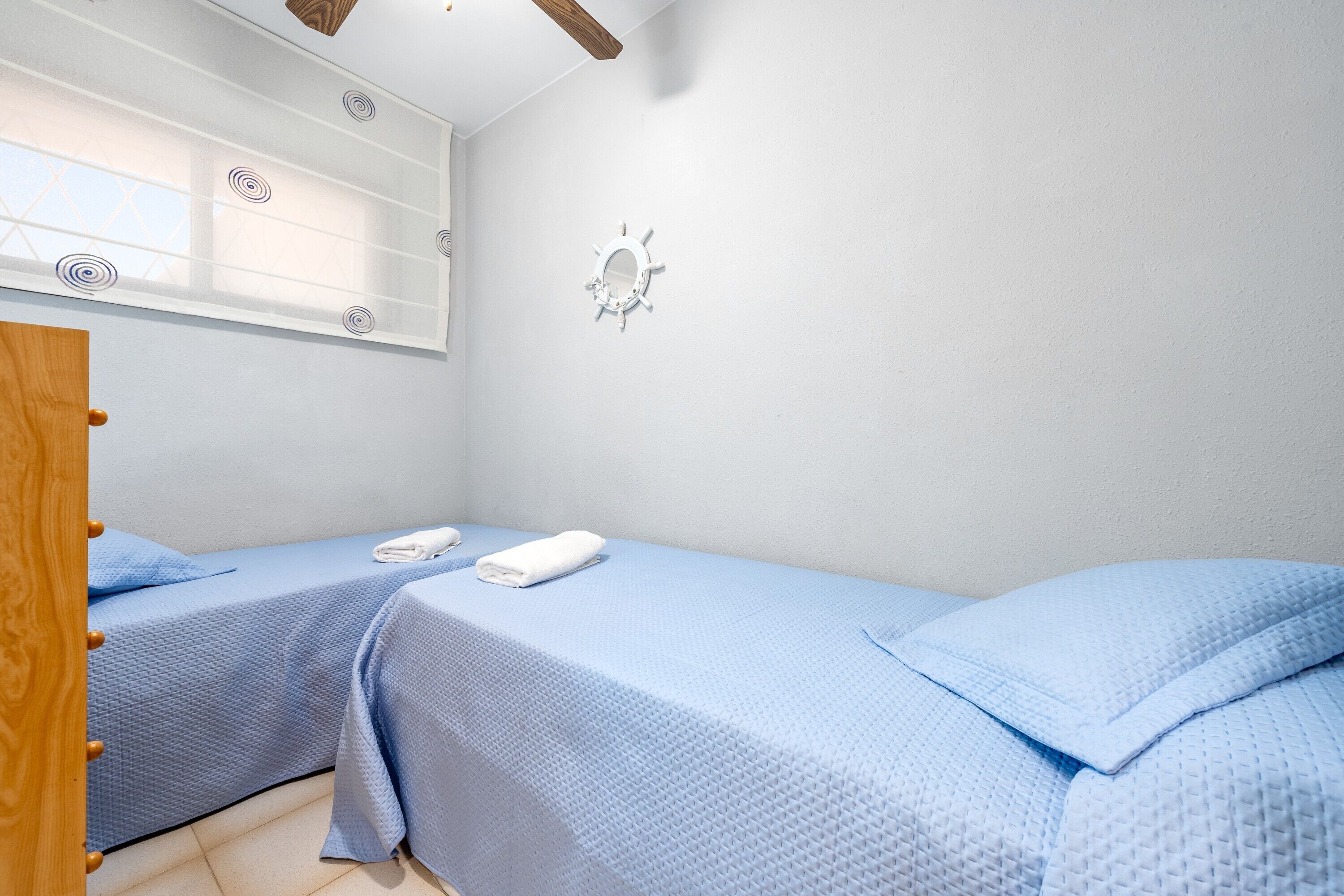 Una camera da letto con due letti, un armadio in legno, uno specchio e una finestra con persiane.