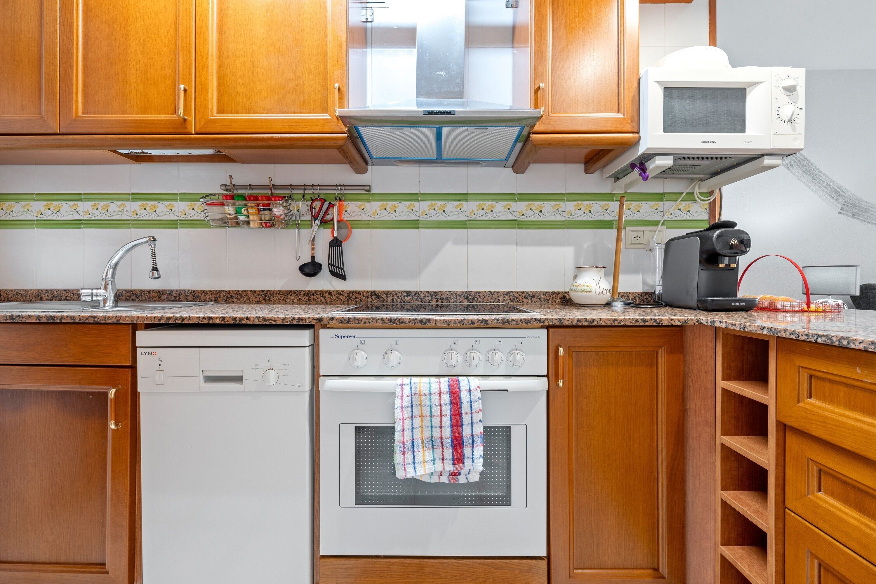 Una cocina con armarios de madera, lavavajillas, horno, microondas y cafetera.