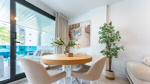 A modern living room with a round wooden table, beige chairs, a potted plant, and a beach-themed wall art. - Apartment 'Jardines De Las Lagunas' with Mountain View, Wi-Fi and Air Conditioning (Las Lagunas de Mijas)
