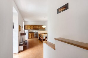 A hallway with a wooden floor, a kitchen area with wooden cabinets, and a dining table with chairs.
