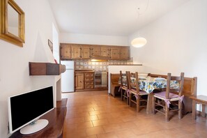 A kitchen with wooden cabinets, a dining table with chairs, and a TV on a stand.