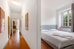 A hotel room with a bed, a window with curtains, a door, and a hallway with a tiled floor.