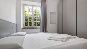 A bedroom with a bed, a window with curtains, a radiator, and a wardrobe.