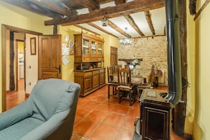 Un intérieur rustique avec des poutres apparentes, un coin repas comprenant une table et des chaises, un buffet et un radiateur.