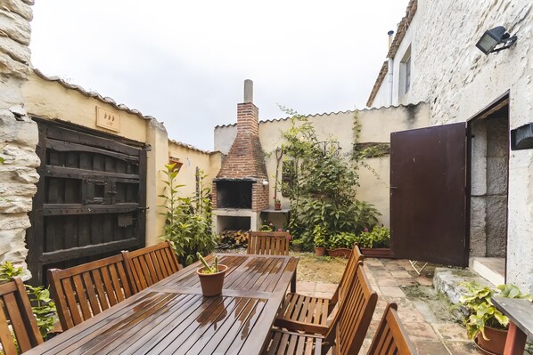 Un patio con una mesa y sillas de madera, una chimenea de ladrillo y plantas en macetas.