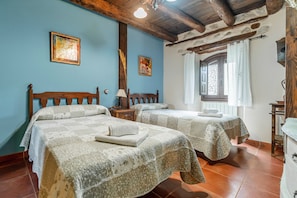 Une chambre avec deux lits, un mur en pierre, des poutres en bois et une fenêtre avec un rideau.