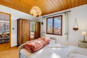 Un dormitorio con cama, armario de madera, ventana con vistas a casas y una lámpara colgante.