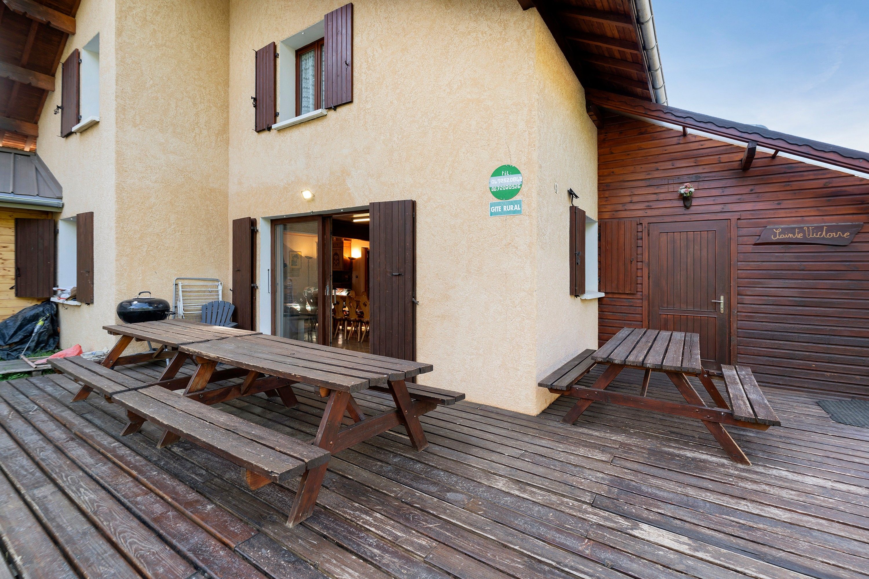 A rustic wooden deck with picnic tables, a wooden door, and a sign indicating a rural setting.