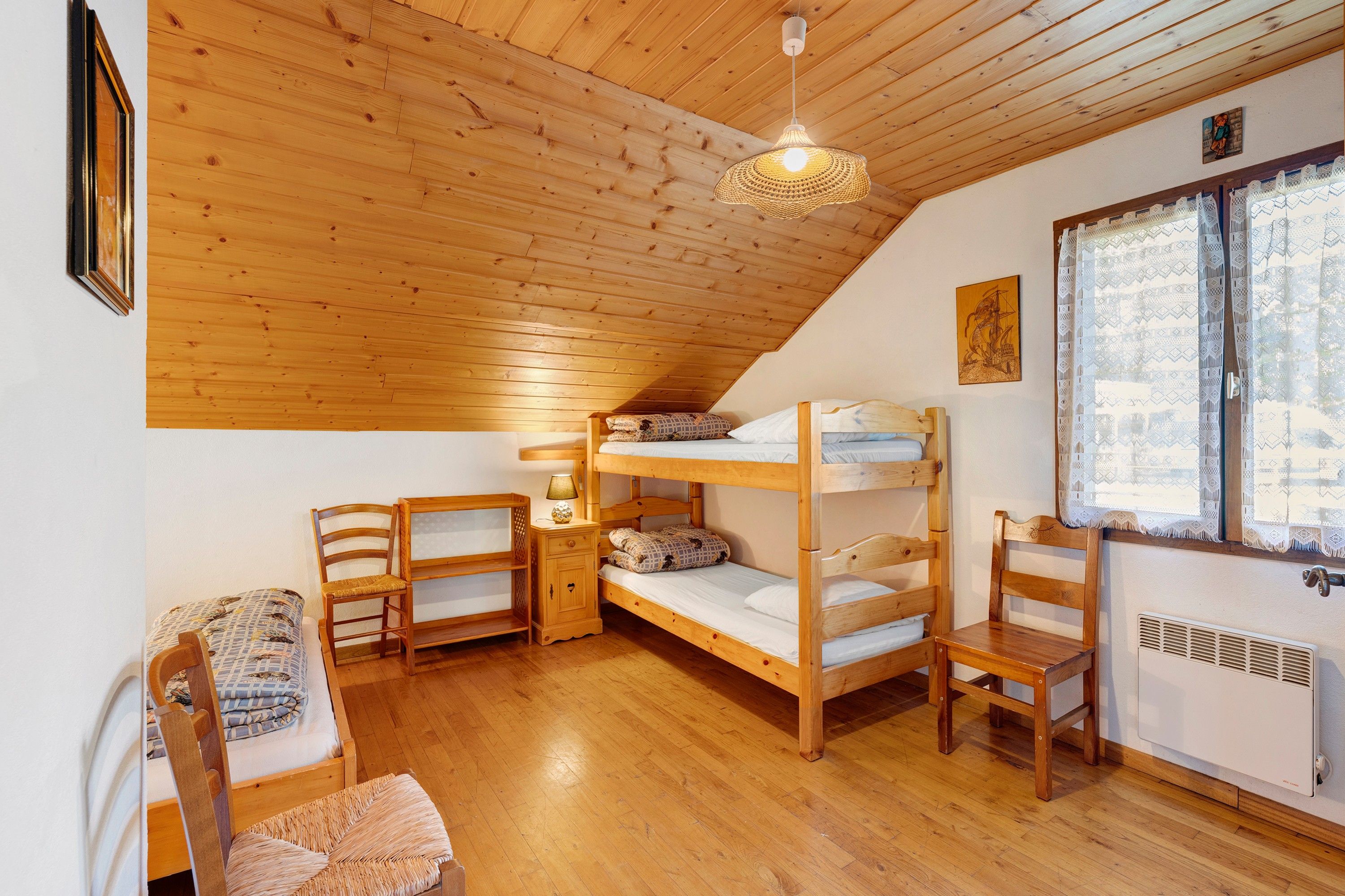 A cozy attic bedroom with wooden bunk beds, a small table with a lamp, a chair, and a radiator.