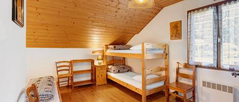 A cozy attic bedroom with wooden bunk beds, a small table with a lamp, a chair, and a radiator.