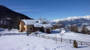Paisaje nevado con una casa de madera y una montaña al fondo.