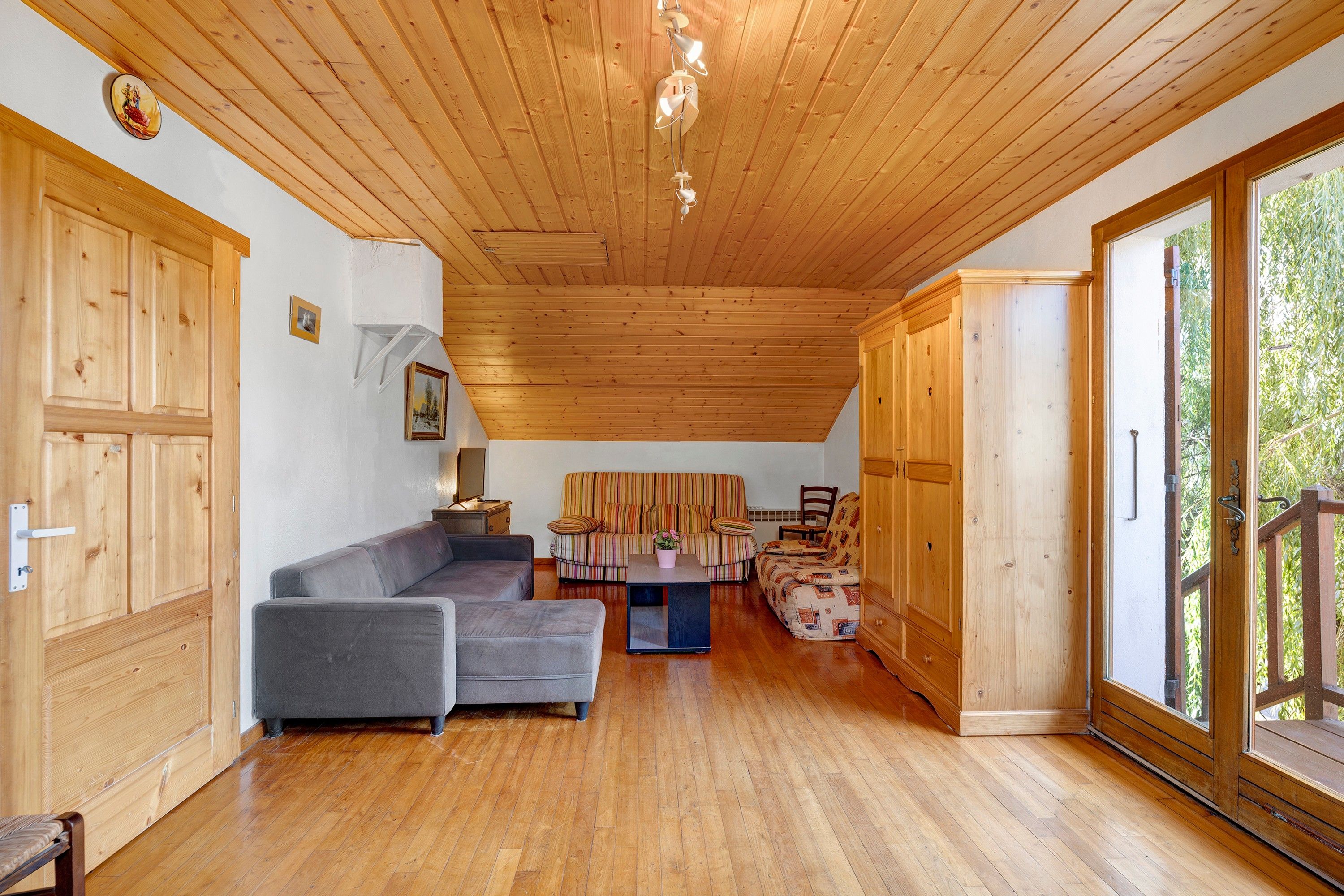 Un vaste espace de vie doté d’un plancher en bois, d’un canapé gris, d’un fauteuil à rayures et d’une armoire en bois.