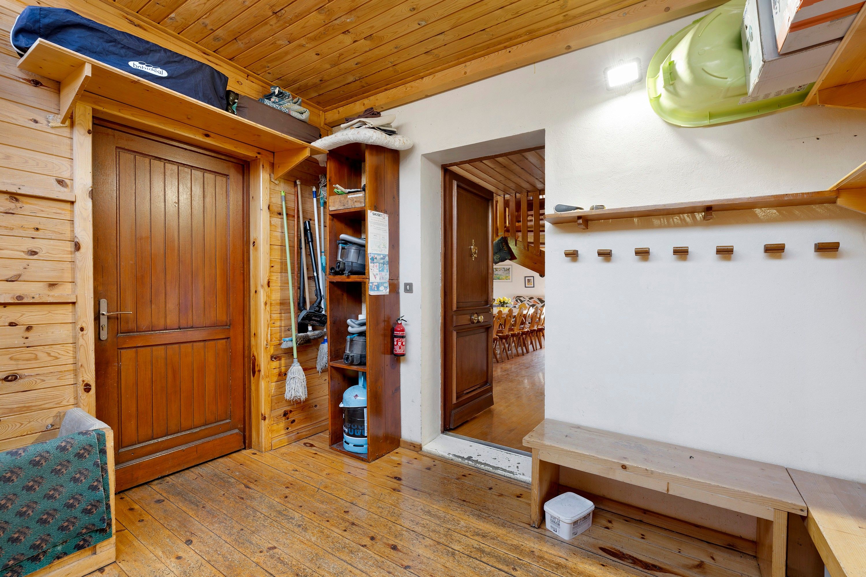 A wooden interior with a door, shelves with cleaning supplies, a fire extinguisher, and a bench.