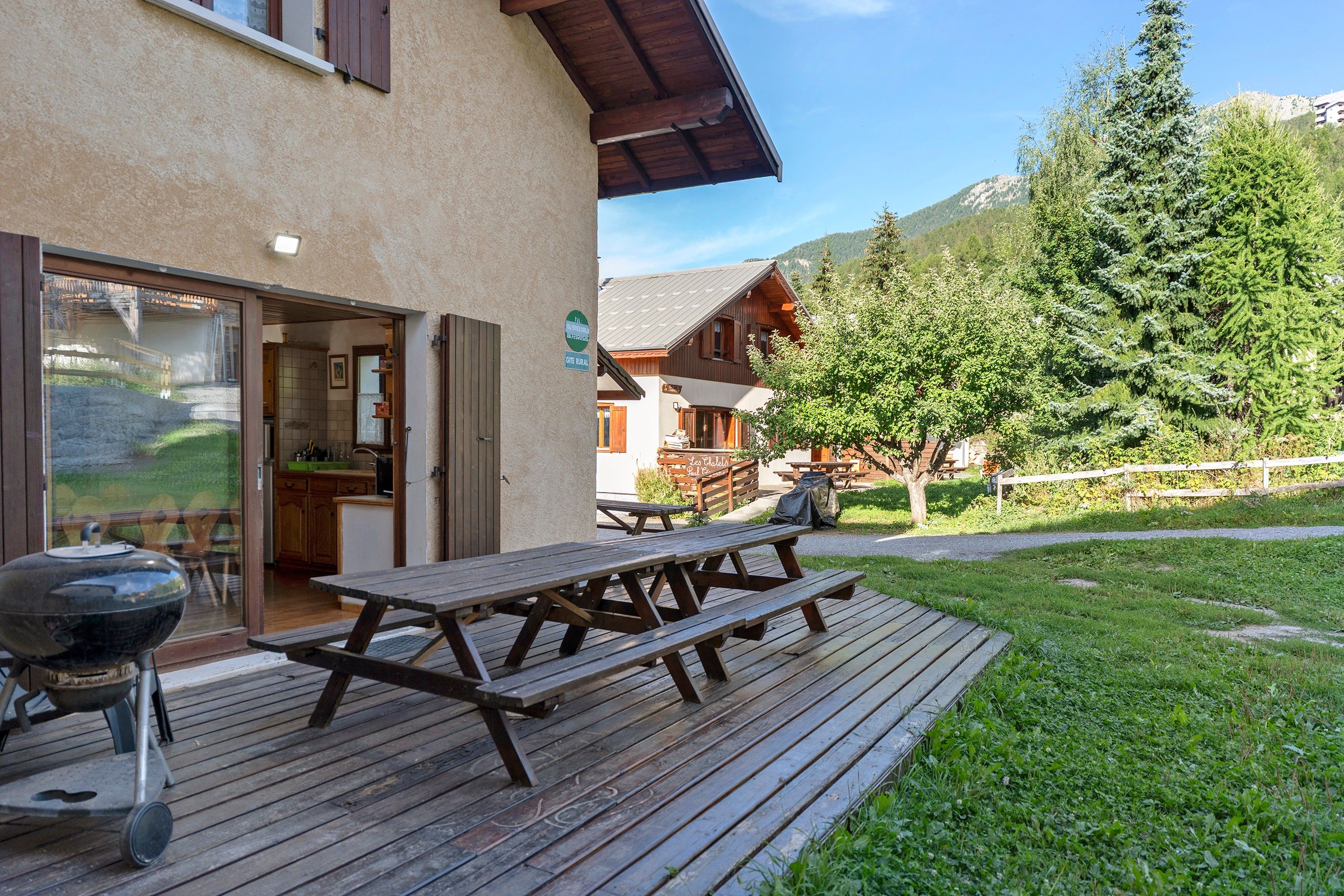 A wooden deck with picnic tables, a barbecue grill, and a mountain view.