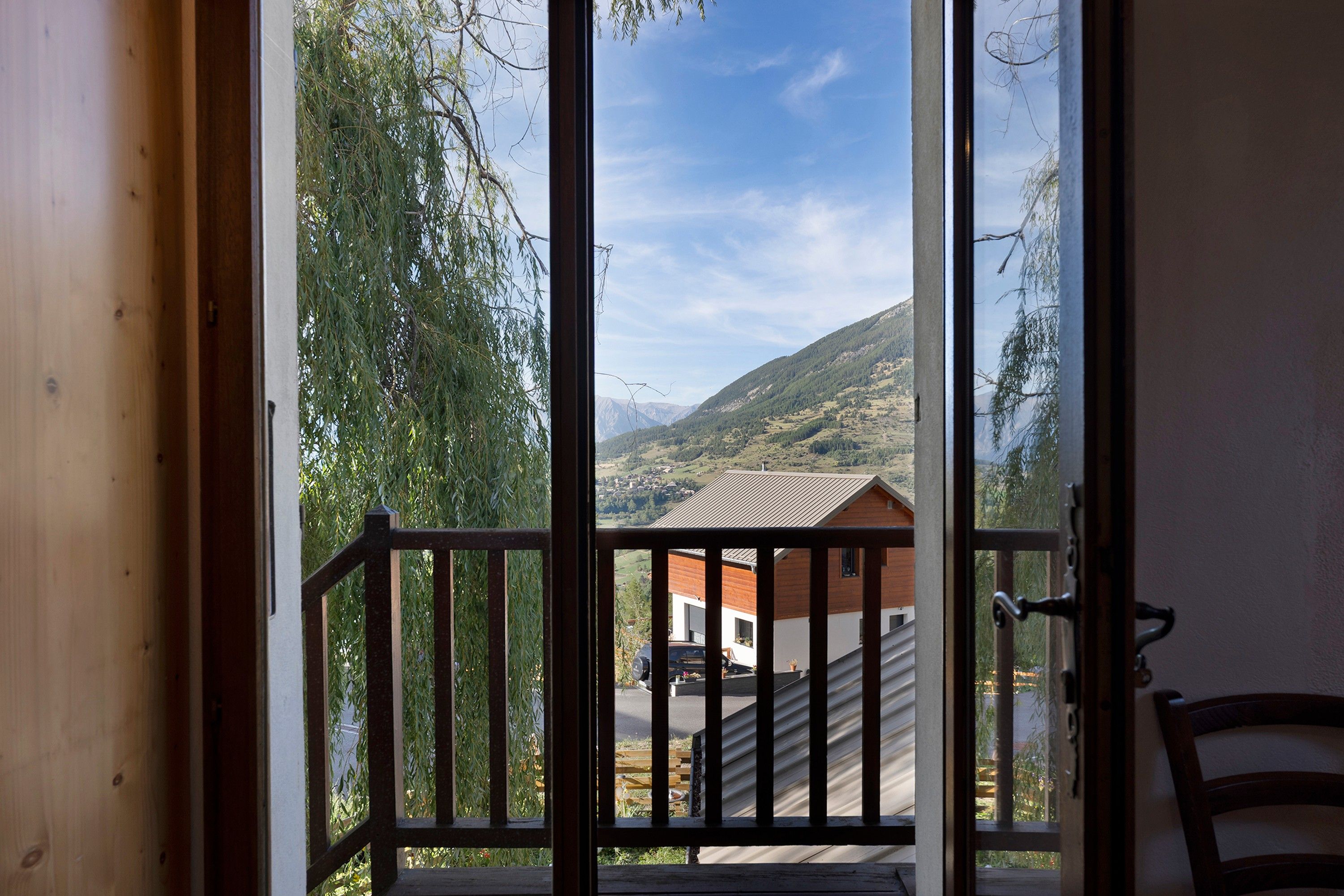Een houten balkon met uitzicht op een berglandschap en een gebouw eronder.